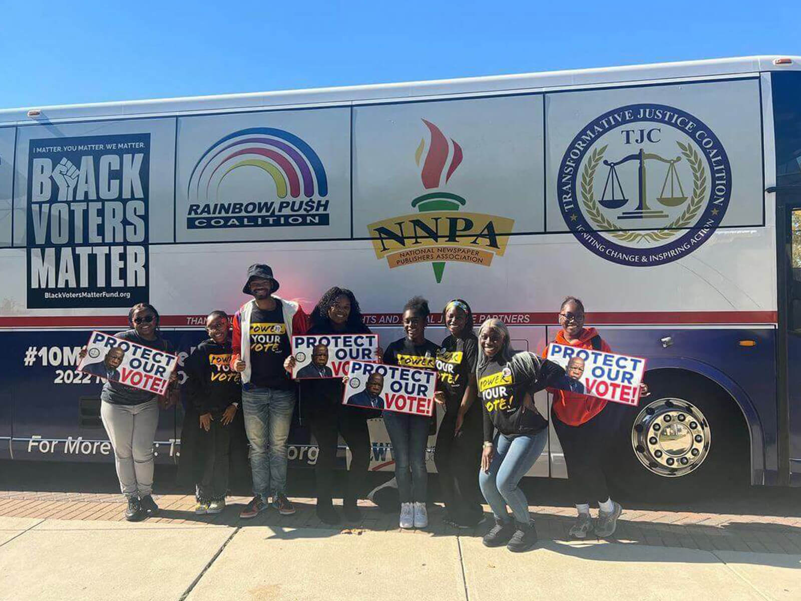 Several people gather in front of a bus, each holding signs that convey their thoughts and support for a cause.