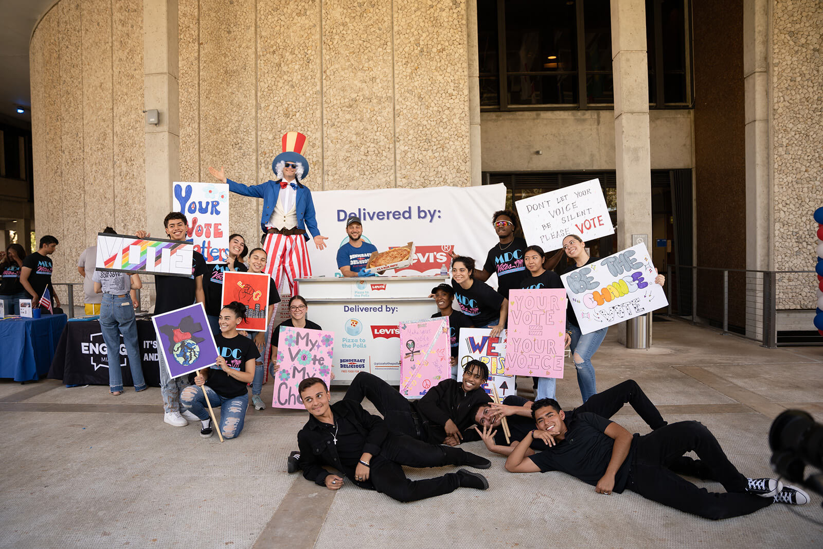 A cheerful gathering of people displaying signs, all posing together for a group photo.